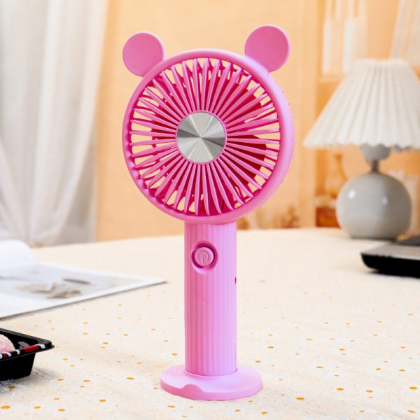 Pink rechargeable handheld fan with round ears, ribbed handle and desktop base